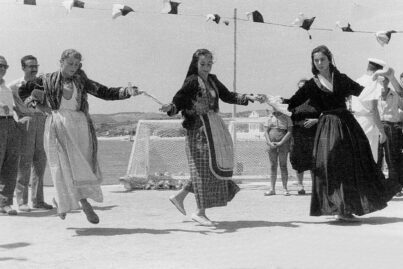 Una fotografía en blanco y negro de tres mujeres bailando en traje folclórico griego